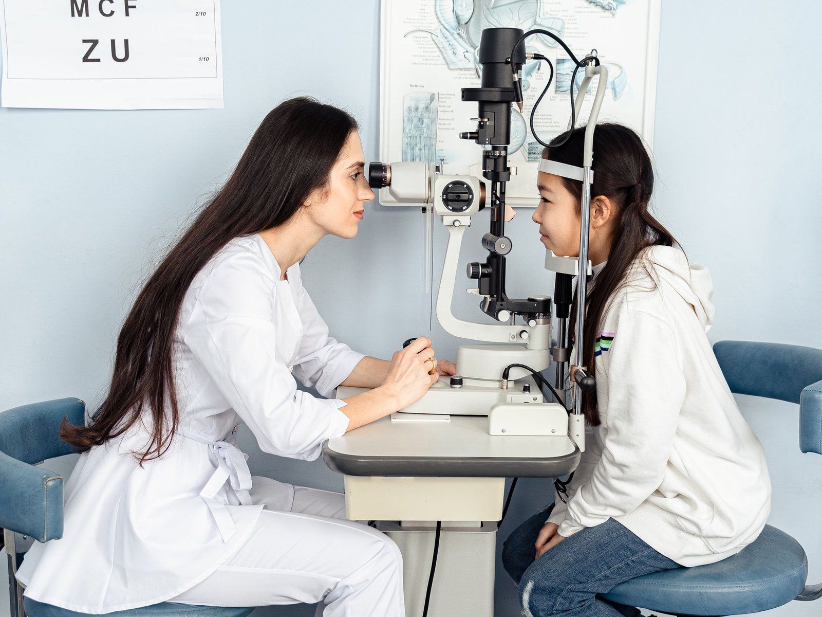 An eye doctor examines a young patient at a slit lamp in a clinic room.