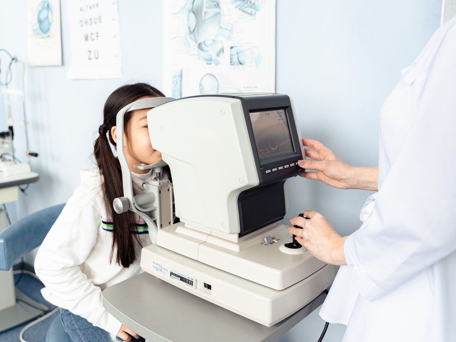 A young patient looks into an autorefractor while an optometrist adjusts the device.